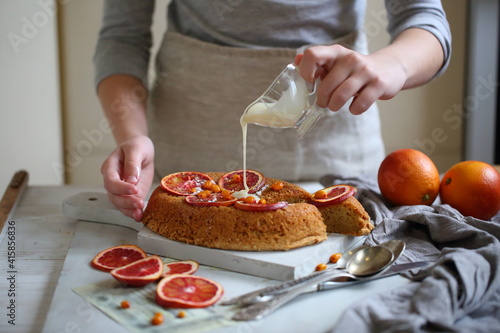 Children's hands sprinkle icing sugar through a sieve on a pie with oranges © Pretti