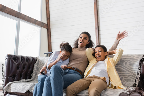 thrilled african american family watching movie on sofa at home