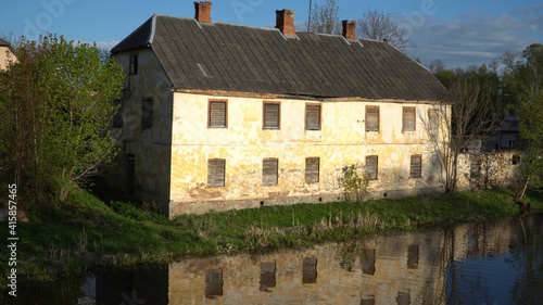 An old, abandoned house with covered windows at the river. The loss of cultural heritage in Europe. The real estate market. Dobele town, Latvia in the spring of 2019.