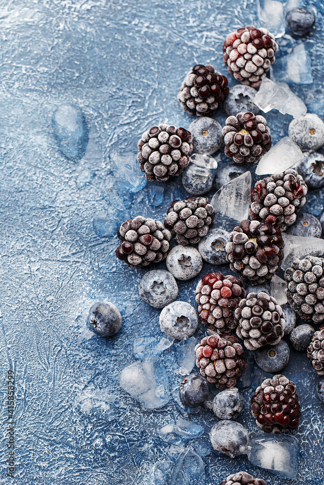 Frozen blueberries and blackberries with crushed ice over dark blue concrete background. Overhead view, copy space. Healthy food background Frozen blueberries and blackberries with crushed ice over dark blue concrete background. Overhead view, copy space. Healthy food background