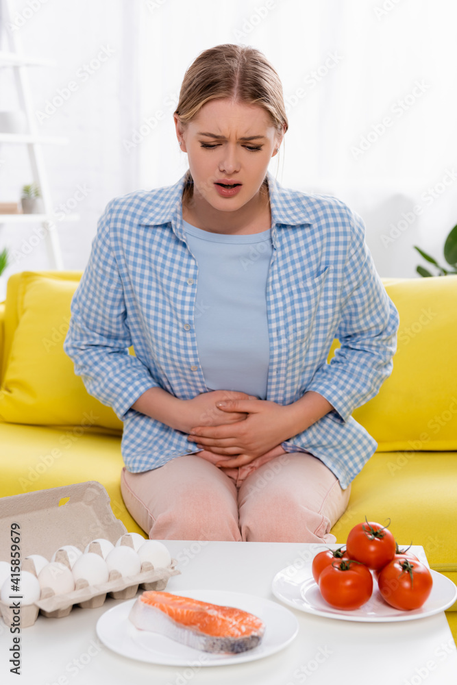 Woman with allergy looking at eggs, tomatoes and salmon on table