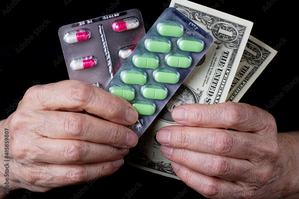 Blister packs with colored pills and US dollar banknotes in elderly woman wrinkled hands on