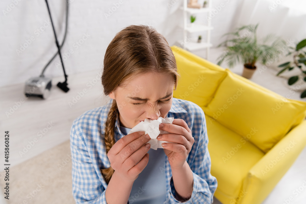 Overhead view of woman suffering from allergy near vacuum cleaner in living room on blurred background Overhead view of woman suffering from allergy near vacuum cleaner in living room on blurred background
