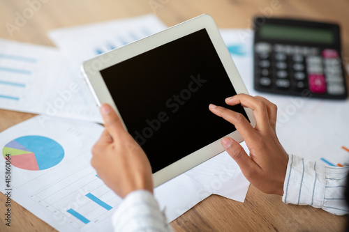 Cropped view of black business lady using tablet computer with blank screen at table with documents, mockup for design
