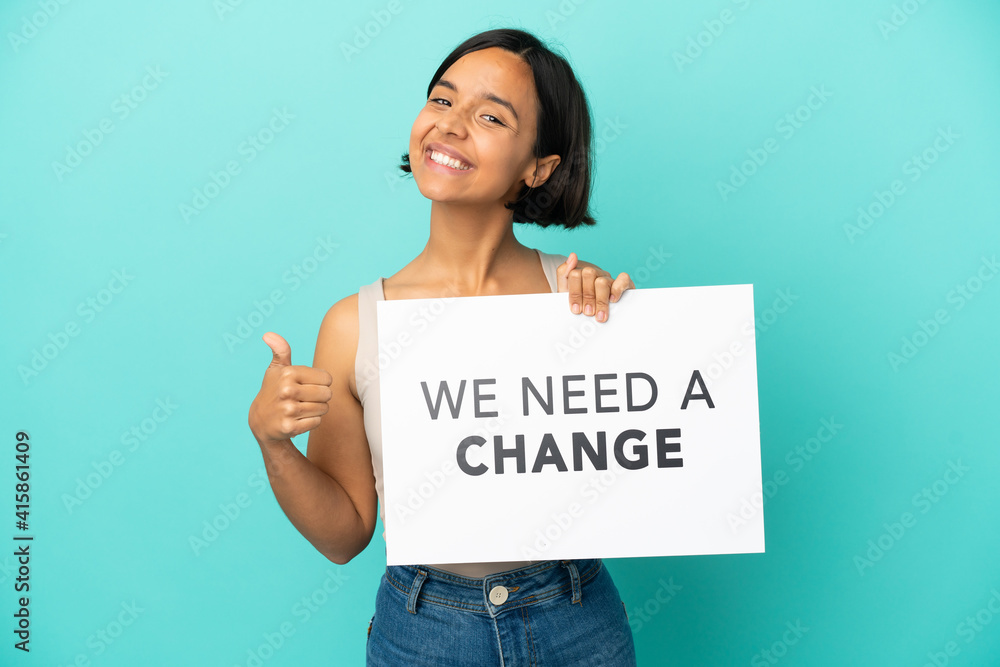 Young mixed race woman isolated on blue background holding a placard with text We Need a Change with thumb up Young mixed race woman isolated on blue background holding a placard with text We Need a Change with thumb up