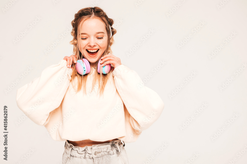Beautiful smiling woman dressed in summer clothes. Sexy carefree model listening music in wireless headphones. Adorable and positive female posing on grey background in studio. Cheerful and happy Beautiful smiling woman dressed in summer clothes. Sexy carefree model listening music in wireless headphones. Adorable and positive female posing on grey background in studio. Cheerful and happy