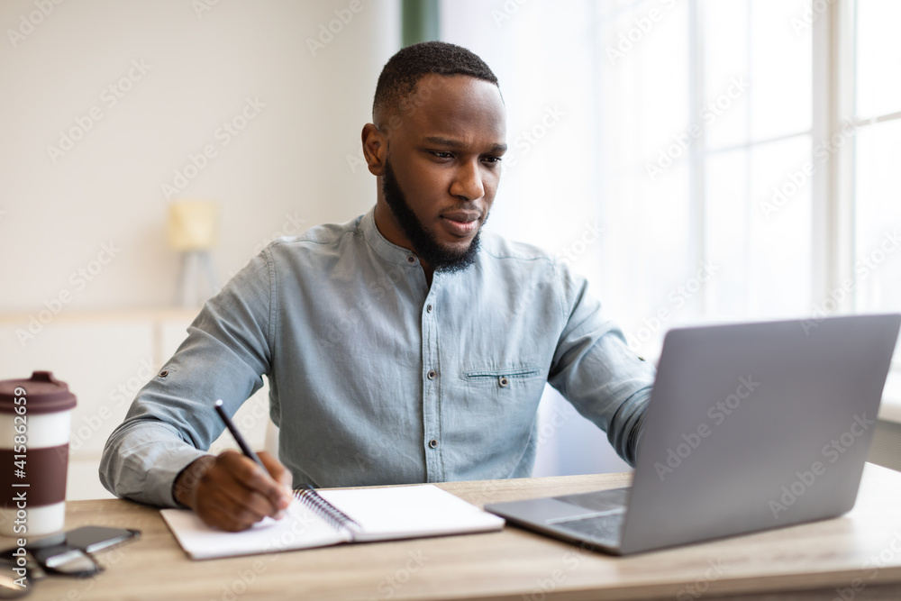 African American Businessman Working On Laptop Taking Notes In Office African American Businessman Working On Laptop Taking Notes In Office