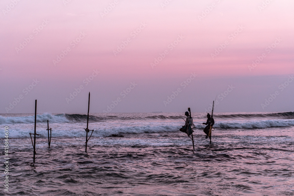 Naklejka premium Lokalni tradycyjni rybacy wędkarze na palach w oceanie na tle zachodzącego słońca.