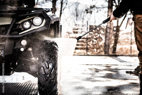 A young man is washing his dirty ATV on the car wash.