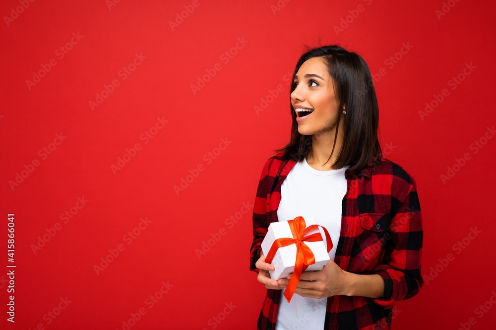 Beautiful happy young brunette woman isolated over colourful background wall wearing stylish casual clothes holding gift box and looking to the side Beautiful happy young brunette woman isolated over colourful background wall wearing stylish casual clothes holding gift box and looking to the side