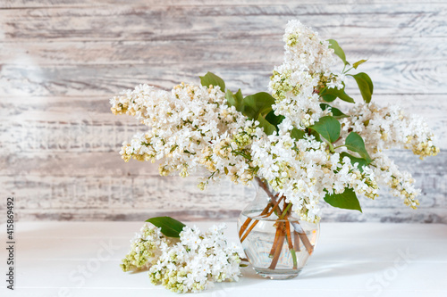 White lilac bouquet in glass vase on wooden table. Spring branches of blooming lilac festive bouquet of flowers with copy space.