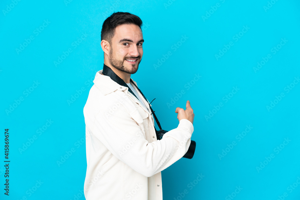 Young photographer man isolated on blue background pointing back Young photographer man isolated on blue background pointing back
