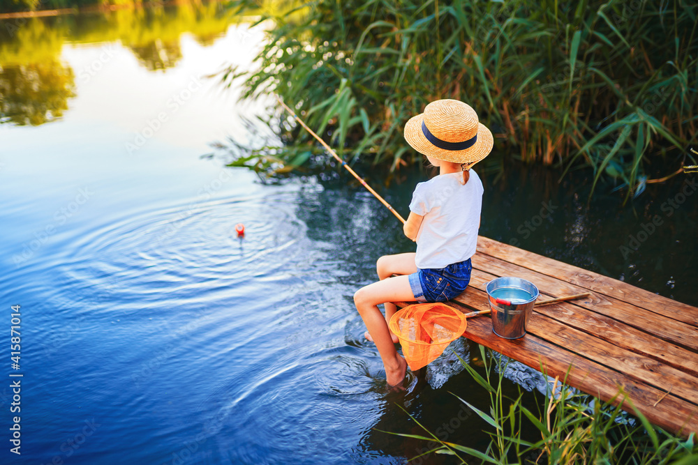 Little boy in straw hat sitting on the edge of a wooden dock and