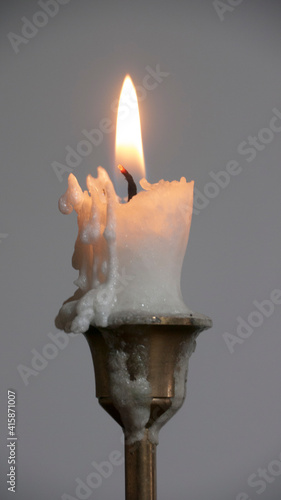 Fotografija Porta velas de latón con vela de cera gastada sobre mesa de madera y pared blanc