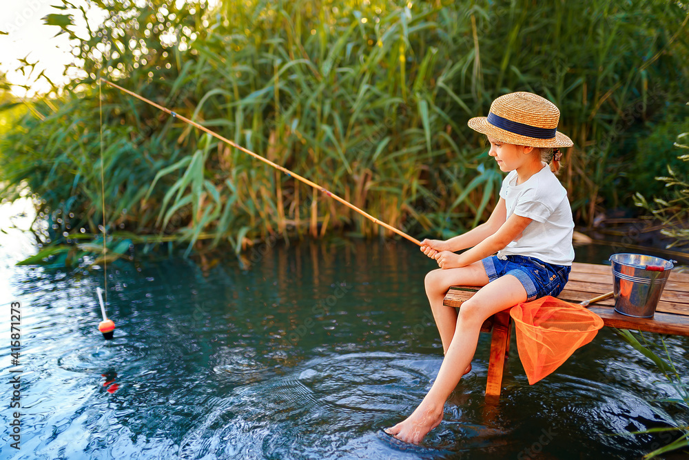 Little boy in straw hat sitting on the edge of a wooden dock and