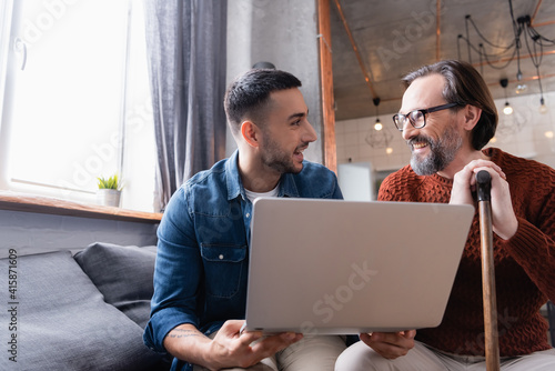 Happy interracial father and son looking at each other near laptop at home