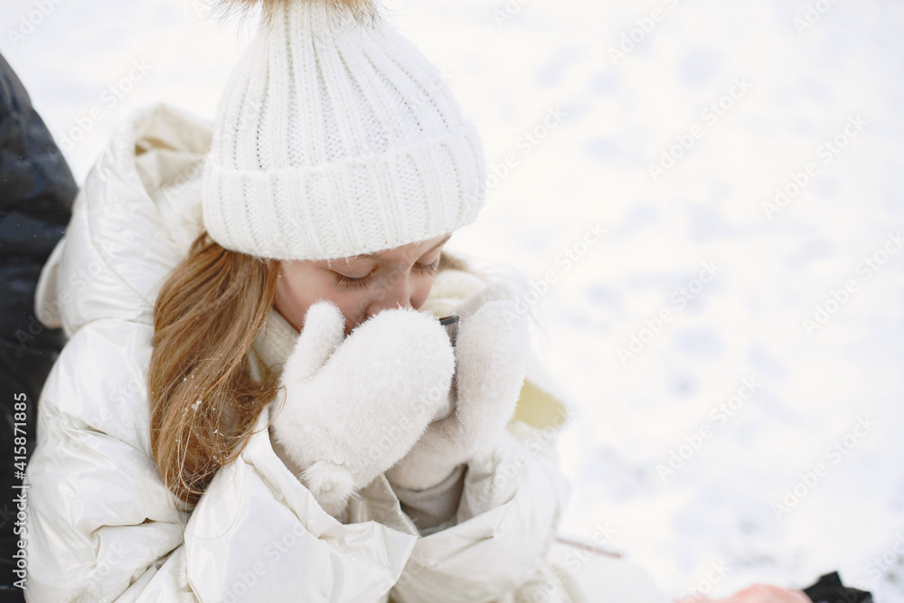 Obraz premium Family in knitted winter hats on family Christmas vacation. Mother with thermos. People sitting on a blanket.