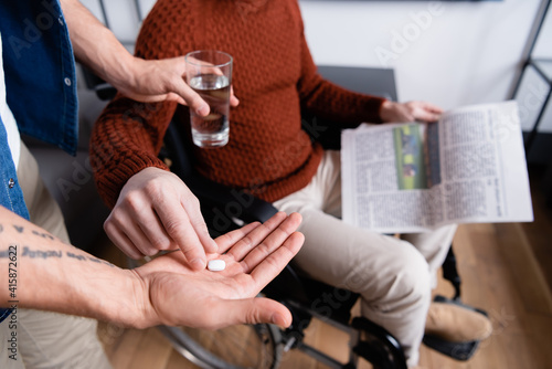 selective focus of disabled man taking pill from son holding glass of water