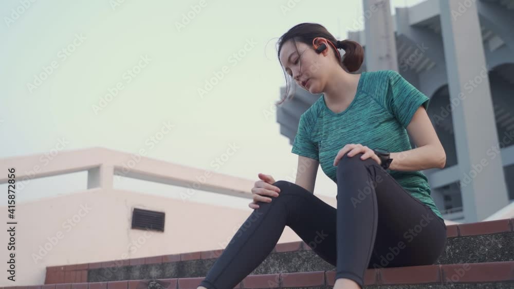 asian athlete woman sitting on stair steps at sport club stadium in evening sunset has knee injury accident. female in sportswear using hands massage legs to relieve pain. asian athlete woman sitting on stair steps at sport club stadium in evening sunset has knee injury accident. female in sportswear using hands massage legs to relieve pain.