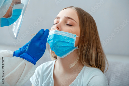 Doctor do PCR test to woman patient. Nurse take saliva sample through nose with cotton swab to check coronavirus covid 19. Medical worker wearing protective mask do PCR test at home or in clinic.