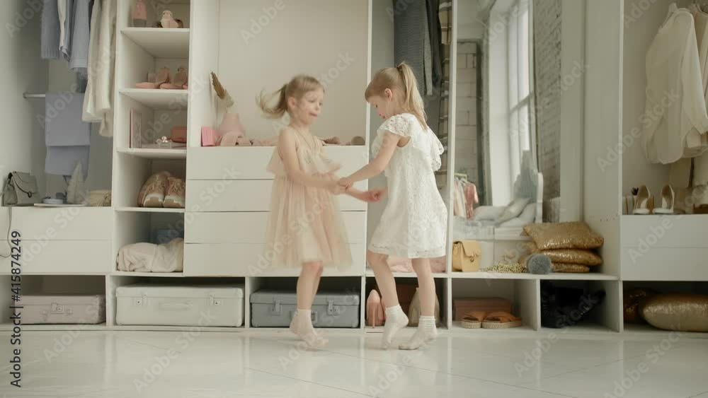 Dancing little girls enjoy new dress in clothing room on backdrop of wardrobe with clothes. Childhood, fashion and style Dancing little girls enjoy new dress in clothing room on backdrop of wardrobe with clothes. Childhood, fashion and style