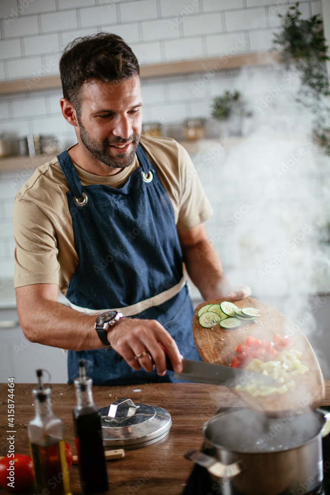 Young man cooking in the kitchen. Happy man preparing delicious food at home.. Young man cooking in the kitchen. Happy man preparing delicious food at home..