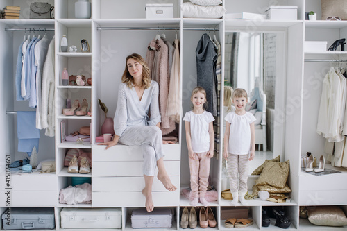 Female wardrobe. Stylish mother, cute twin daughters wearing comfortable home clothes posing in closet. Happy motherhood