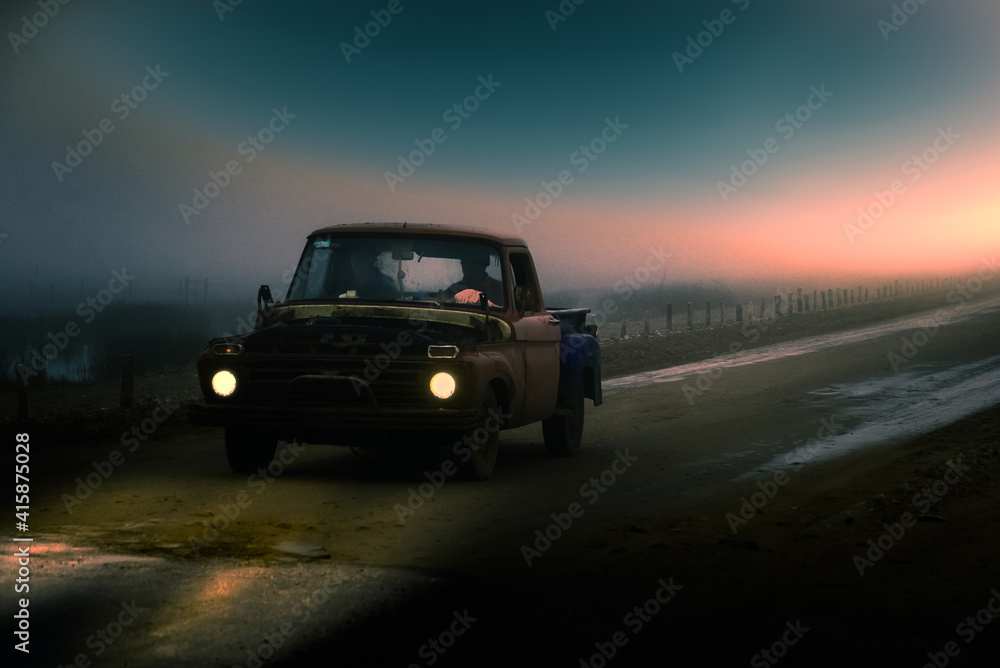antigua pickup deteriorada circula por un camino de tierra, en un clima nublado y brumoso, con dos personas en su interior, mientras cae el sol antigua pickup deteriorada circula por un camino de tierra, en un clima nublado y brumoso, con dos personas en su interior, mientras cae el sol