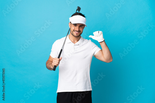 Young handsome man isolated on blue background playing golf and proud of himself