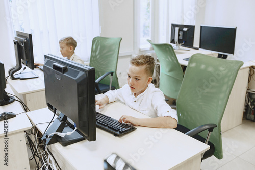 Children learns to work on a computer. Boys are sitting at the table. Schoolboy in a white shirt.