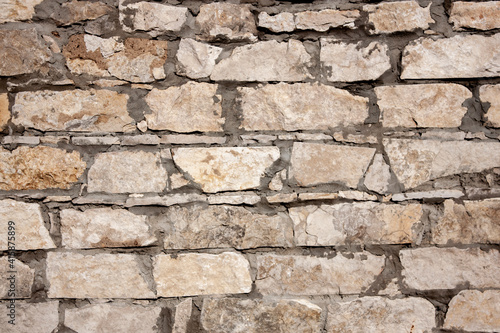 Fragment of a wall made of stones of different sizes. Close-up of a rough stone wall. Part of a stone wall on a sunny day.
