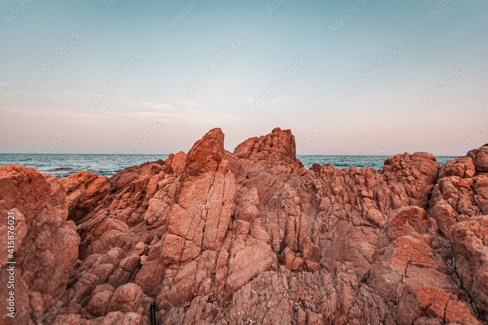 Beautiful sunset seascape in Italy, Sardinia island. Red and pink rocks, wind erosion, geology stratification, air oxidation. Teal and orange lighting, endless horizon and soft pastel colored clouds.