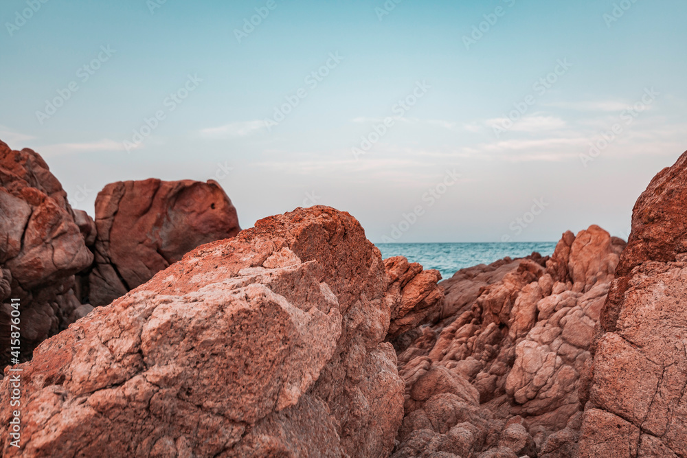 Beautiful sunset seascape in Italy, Sardinia island. Red and pink rocks, wind erosion, geology stratification, air oxidation. Teal and orange lighting, endless horizon and soft pastel colored clouds.