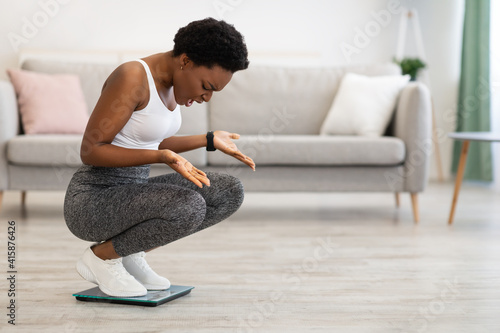 Frustrated Black Lady Looking At Scales After Weight Gain Indoor