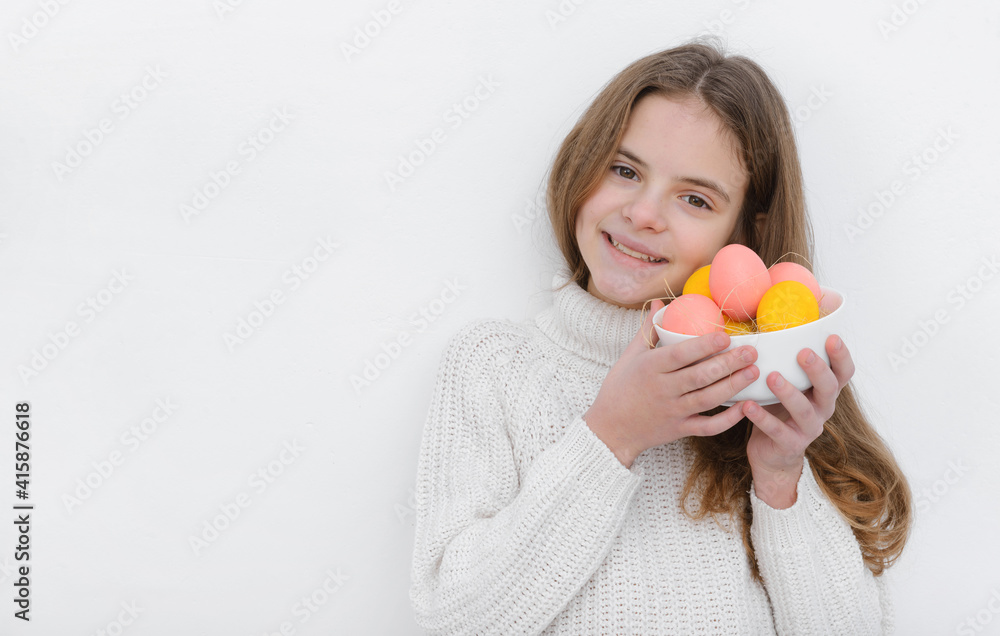 European girl with pink and yellow Easter eggs in her hands, wearing a white sweater against a white wall European girl with pink and yellow Easter eggs in her hands, wearing a white sweater against a white wall