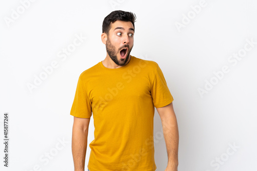 Young handsome man with beard isolated on white background doing surprise gesture while looking to the side