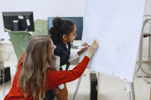 Child in computer science class. African girl standing near school board for presentation. Teacher with her student.