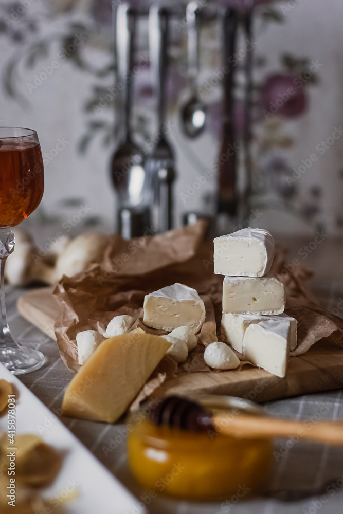 Delicious cheeses on a board with honey and wine on a paper background