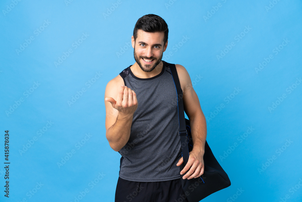 Young sport man with sport bag isolated on blue background inviting to come with hand. Happy that you came Young sport man with sport bag isolated on blue background inviting to come with hand. Happy that you came