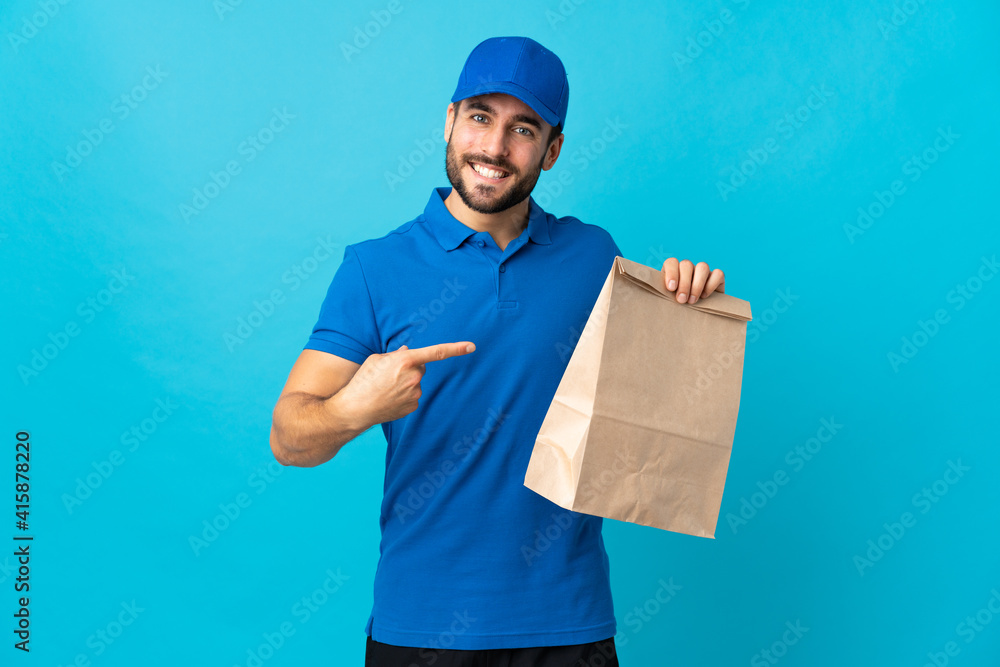 Delivery man with beard isolated on blue background and pointing it Delivery man with beard isolated on blue background and pointing it