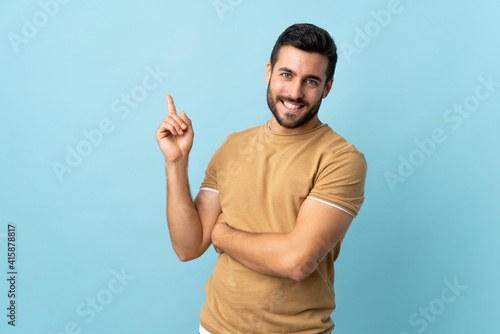 Young handsome man with beard over isolated background happy and pointing up