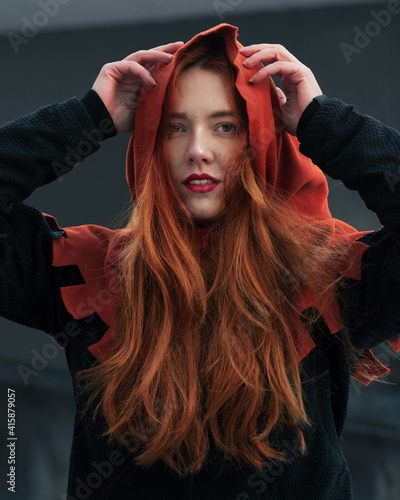 Obraz na płótnie Portrait of beautiful red-haired young woman in hood looking at camera. Girl in the image of Red woman. w salonie
