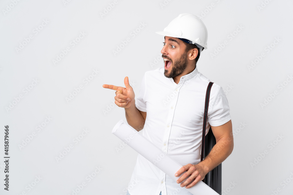 Young architect man with helmet and holding blueprints isolated on white background pointing finger to the side and presenting a product Young architect man with helmet and holding blueprints isolated on white background pointing finger to the side and presenting a product