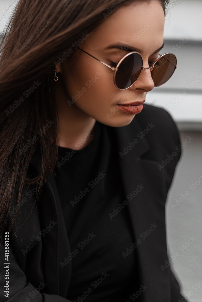 Fresh portrait of cute beautiful young woman in round fashionable sunglasses  in black stylish blazer with sexy lips outdoors in city. Attractive girl  fashion model in casual elegant business clothes. Photos