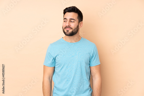Caucasian handsome man isolated on beige background having doubts while looking side