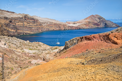 Rocks and multicolored ocher sands, blue sea and boat at the eastern point of the island of Madeira and the point of saint lorenzo (Ponta de São Lourenço)