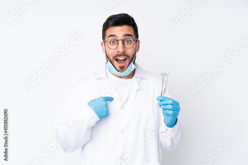 Dentist man holding tools isolated on white background with surprise facial expression