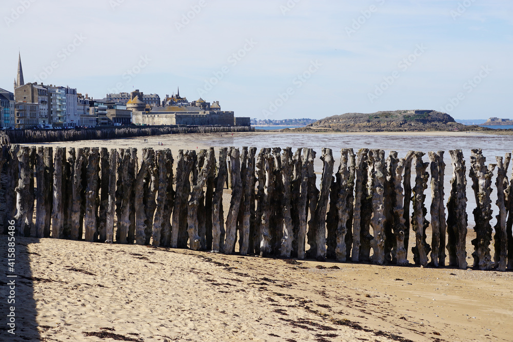 view of the beach, wooden wave breaker and town of St Malo, France