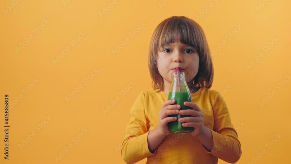 Happy Children drink a green smoothies. Cute kids with Healthy breakfast in yellow background Happy Children drink a green smoothies. Cute kids with Healthy breakfast in yellow background