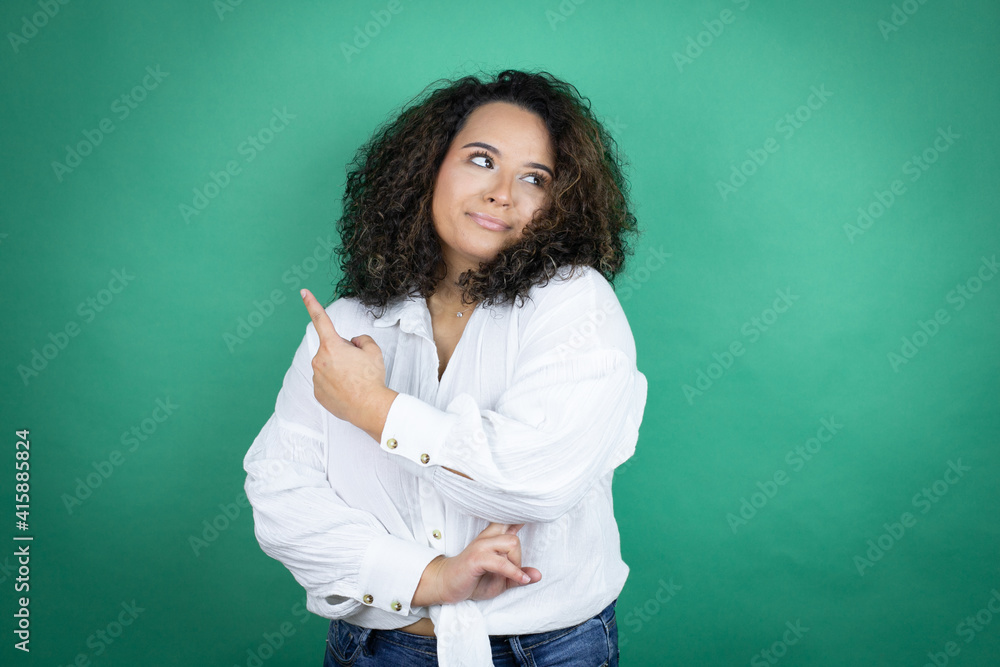 Young african american girl wearing white shirt over green background confused and pointing with hand and finger to the side